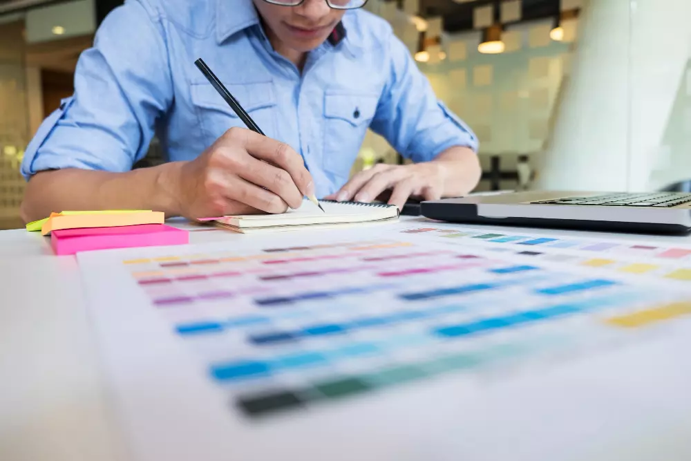 Diseñador gráfico trabajando en una mesa con muestras de colores y bocetos para nuestros productos impresos.