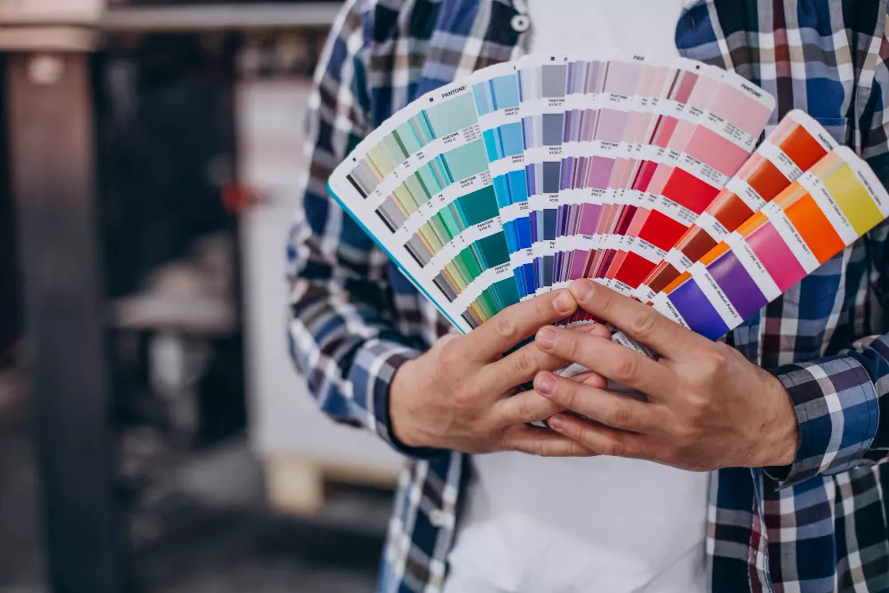 Persona sosteniendo un abanico de muestras de colores Pantone, representando la selección precisa y estandarizada de colores en proyectos de diseño gráfico e impresión.