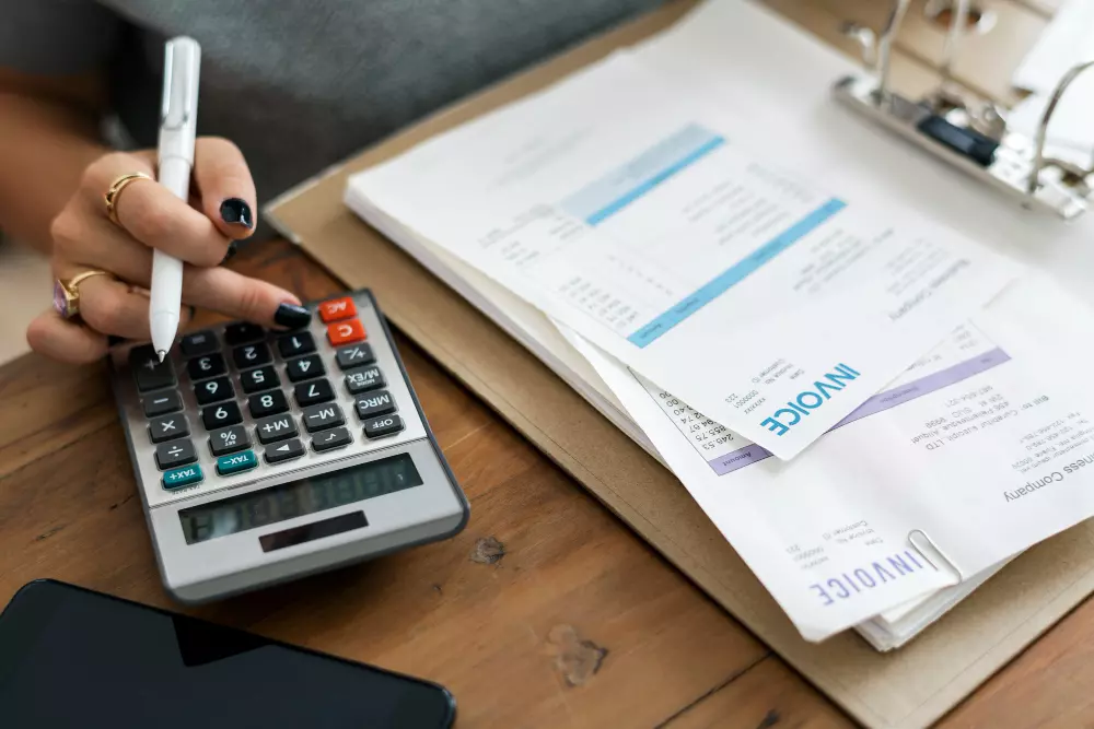 Una persona utilizando una calculadora y revisando facturas impresas en los talonarios autocopiativos, una herramienta clave para llevar un control eficiente de las transacciones comerciales.