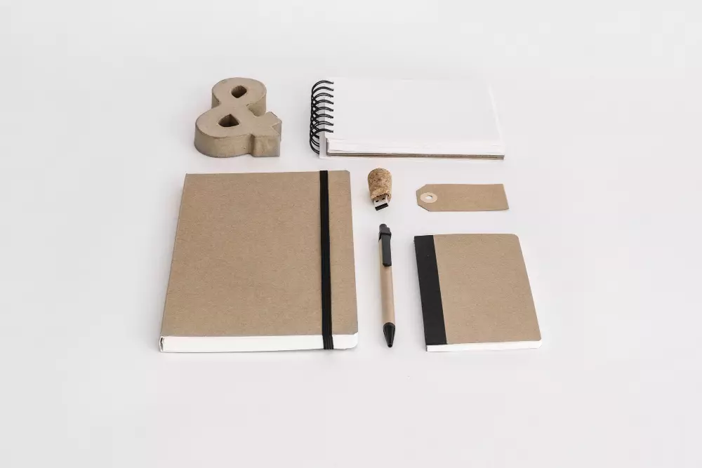 Conjunto de material corporativo personalizado y ecológico, incluyendo cuadernos, bolígrafo y etiquetas, que demuestra los beneficios de personalizar material corporativo para crear una imagen de marca sostenible y profesional.